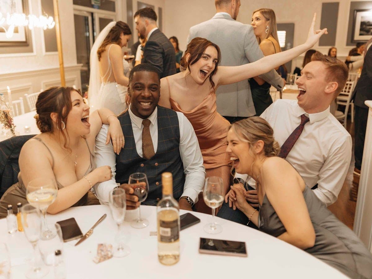 A wedding party laughing together around a reception table.